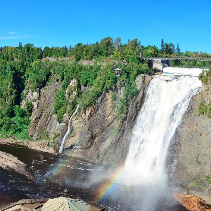 Vue panoramique du parc de la Chute-Montmorency, mettant en vedette l'impressionnante chute Montmorency entourée d'une verdure luxuriante, avec un pont et des plateformes d'observation surplombant la cascade en cascade.