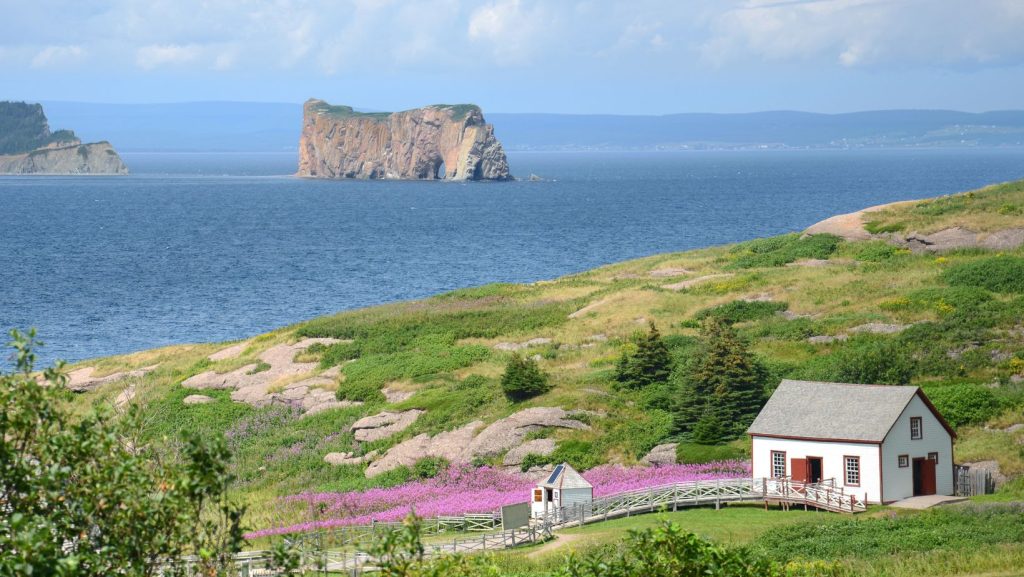 Vue panoramique du rocher Percé, une formation calcaire massive s'élevant de la mer, avec l'île Bonaventure en arrière-plan. Ces sites naturels emblématiques sont entourés par les eaux bleu clair du golfe du Saint-Laurent, mettant en valeur la beauté à couper le souffle du littoral québécois.