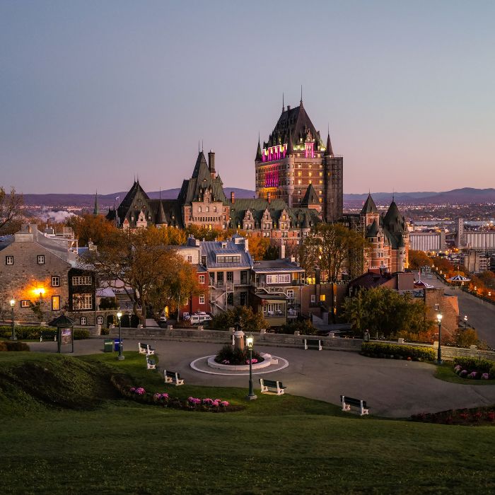 Vue du Vieux-Québec avec ses charmantes rues pavées, ses bâtiments historiques en pierre et un aperçu de l'emblématique Château Frontenac sur fond de ciel bleu.